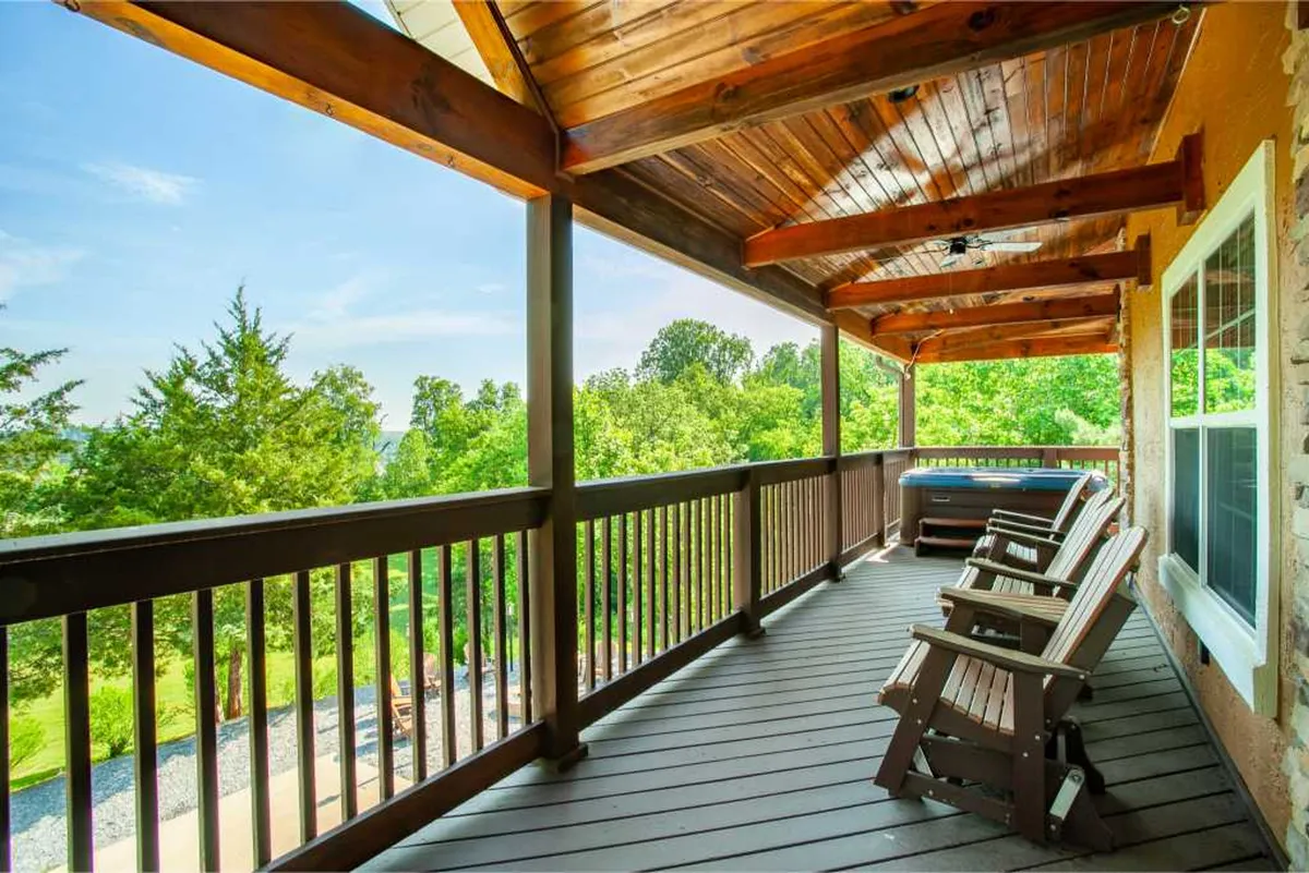 A tranquil wooden deck scene featuring comfortable rocking chairs overlooking lush greenery and an open sky. The deck wraps around the house, offering multiple spots to relax and take in the views, ideal for morning coffee or evening relaxation.