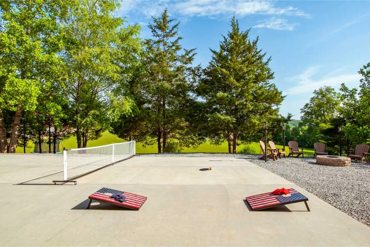 This image captures an active outdoor scene featuring cornhole boards set up on a spacious lawn, comfortable seating arranged around a fire pit, and people gathering and enjoying the outdoors. The setting exudes a casual and friendly atmosphere, ideal for socializing and play.
