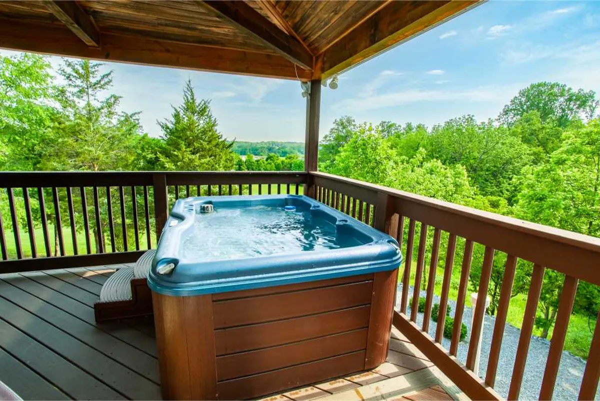 A peaceful scene showcasing a bubbling hot tub on a wooden deck surrounded by lush greenery. The inviting jacuzzi is positioned for optimal views, suggesting moments of relaxation under the sky, whether during the day or while stargazing at night.