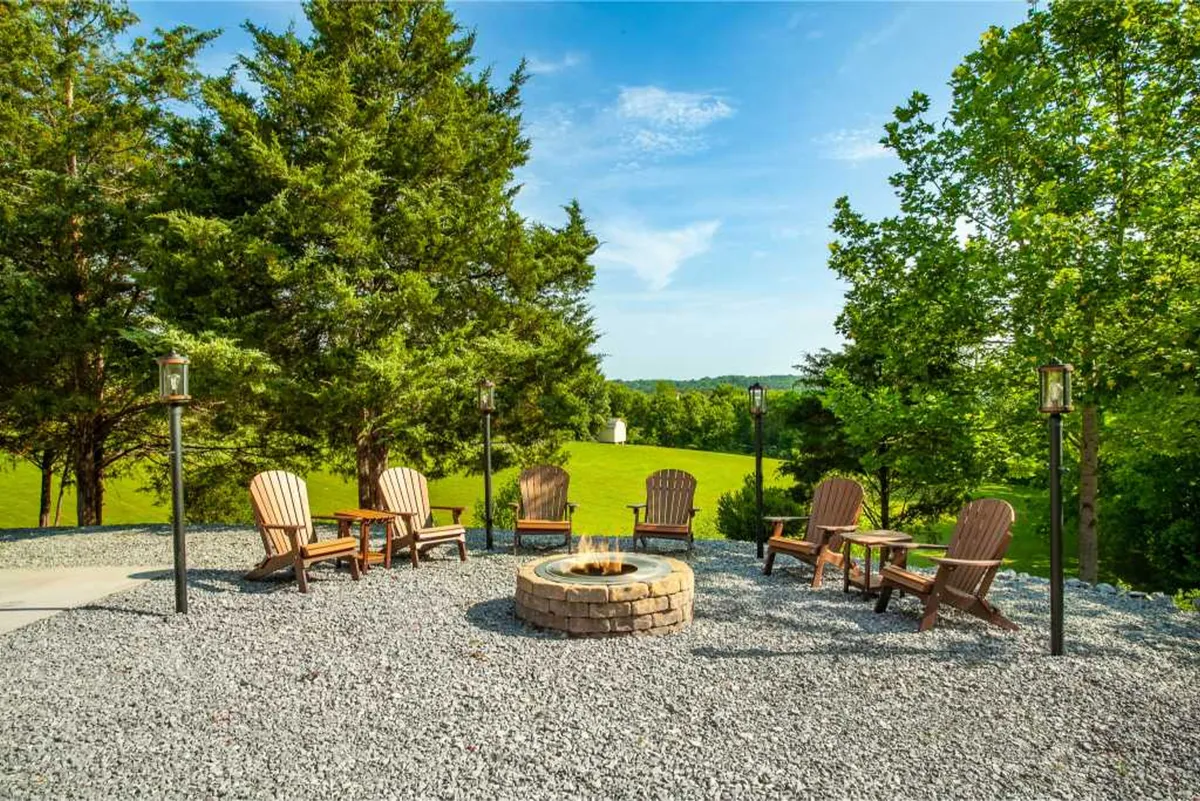 This exterior image features a cozy fire pit encircled by Adirondack chairs, set amidst lush greenery. The scene exudes a communal atmosphere with friends gathered around the fire, drinks in hand, sharing stories and laughter as evening falls.