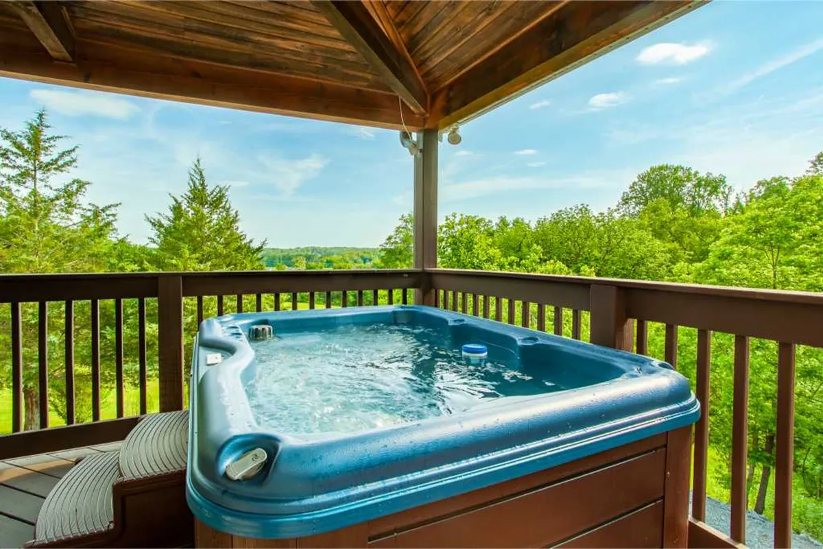 A serene view of the wooden deck featuring a bubbling hot tub, surrounded by trees. The area is designed for relaxation and enjoying the peaceful mountain ambiance, ideal for unwinding after a day of adventure.