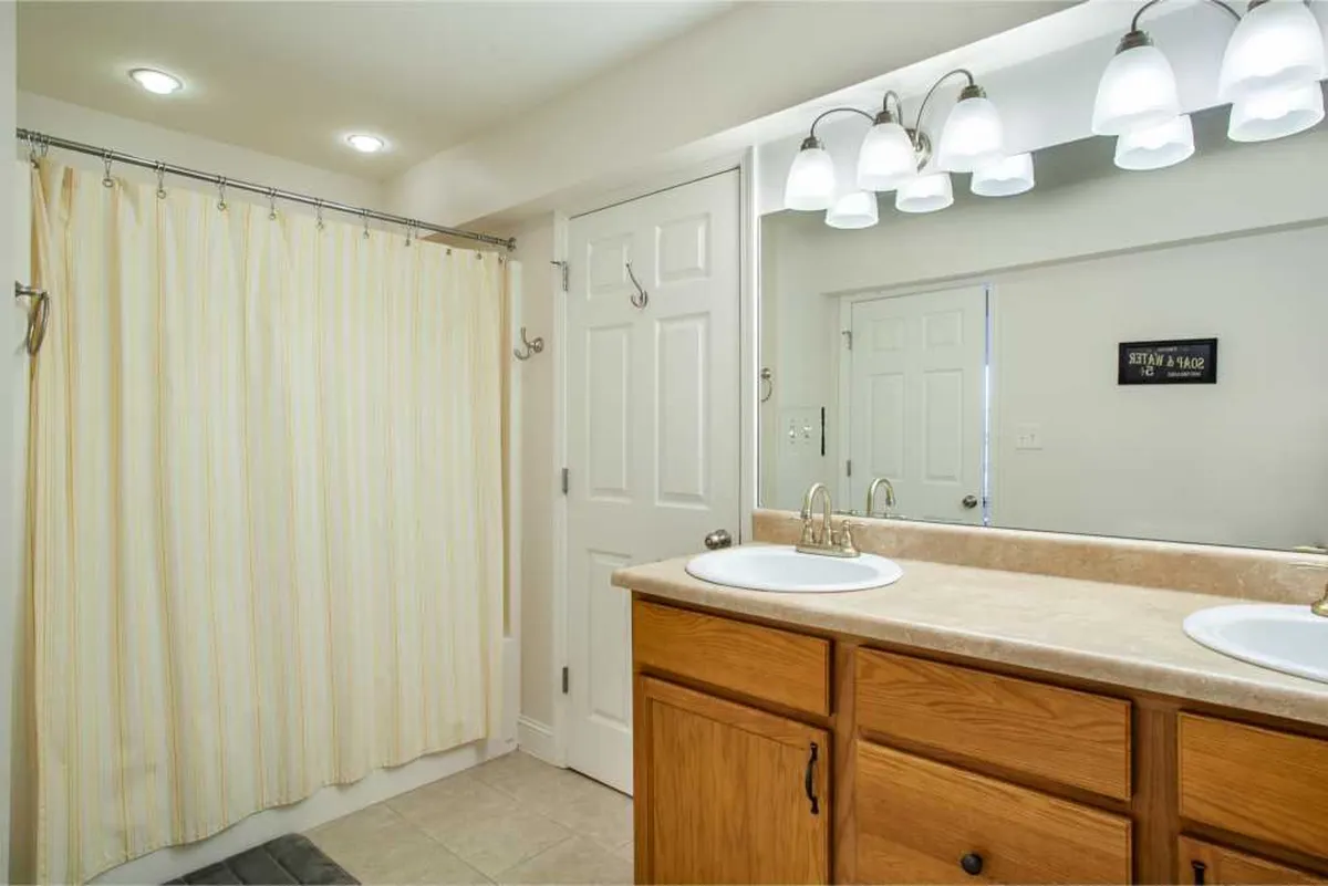 A fresh, bright bathroom with double vanity sinks, a large mirror, stylish light fixtures, and a shower curtain. The space feels clean and inviting—perfect for unwinding at the start or end of the day.