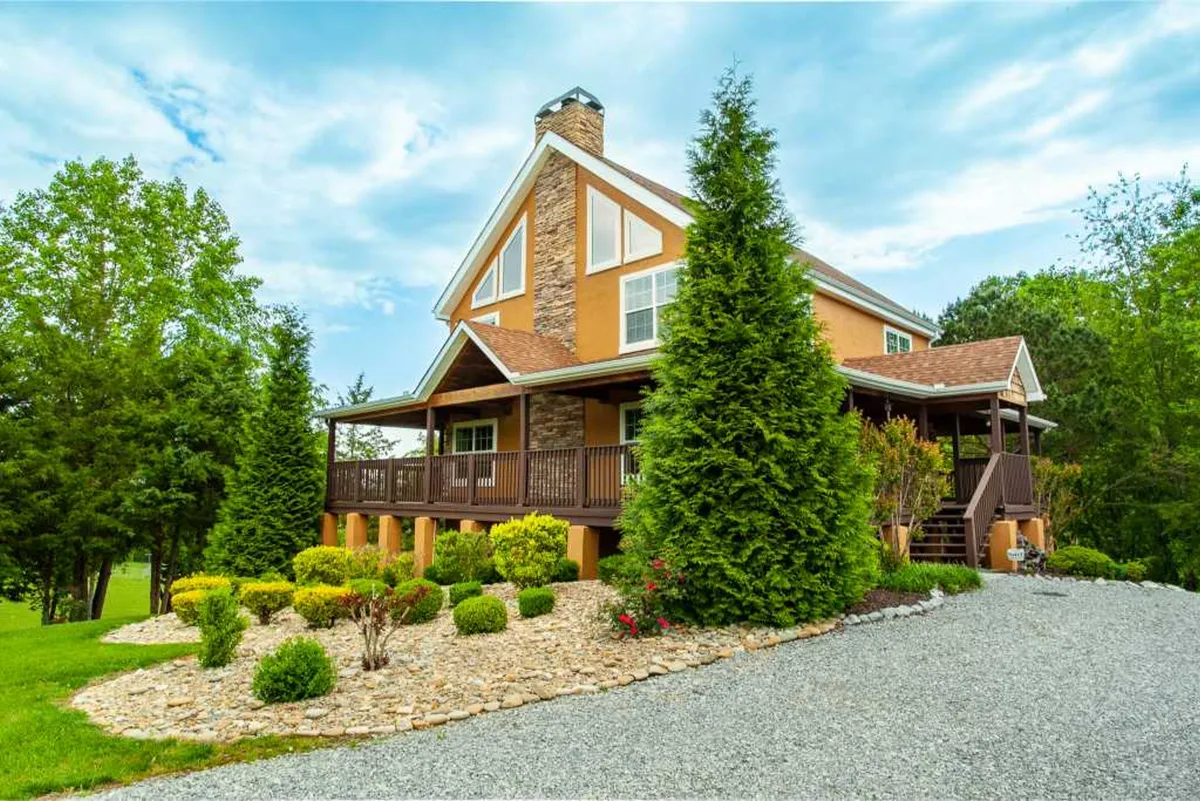 A welcoming exterior view of the house, surrounded by manicured landscaping and a spacious driveway. The porch, basked in golden sunset light, suggests a perfect spot for morning coffee or unwinding as the day ends.