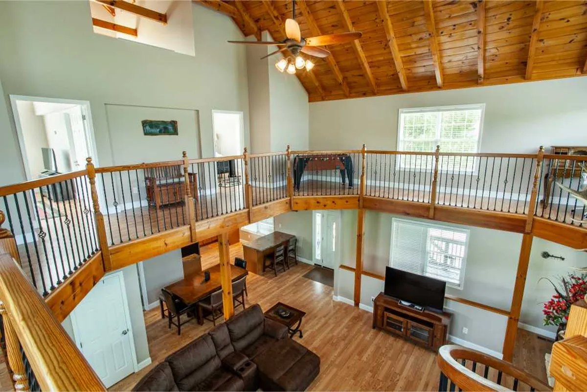 A warm, open-plan living area with a vaulted wooden ceiling, inviting seating, a large dining table, and a visible game area featuring a foosball table. The space is well-lit by natural light and encourages both relaxation and lively gatherings.