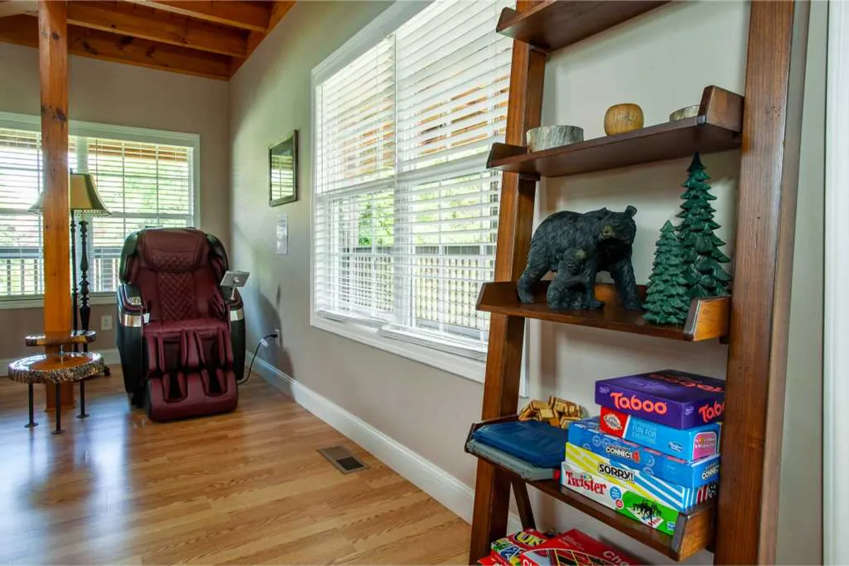 A comfortable corner featuring a high-end massage chair next to a wooden shelf with a variety of board games. The cozy setting invites relaxation and playful downtime after energetic gatherings.